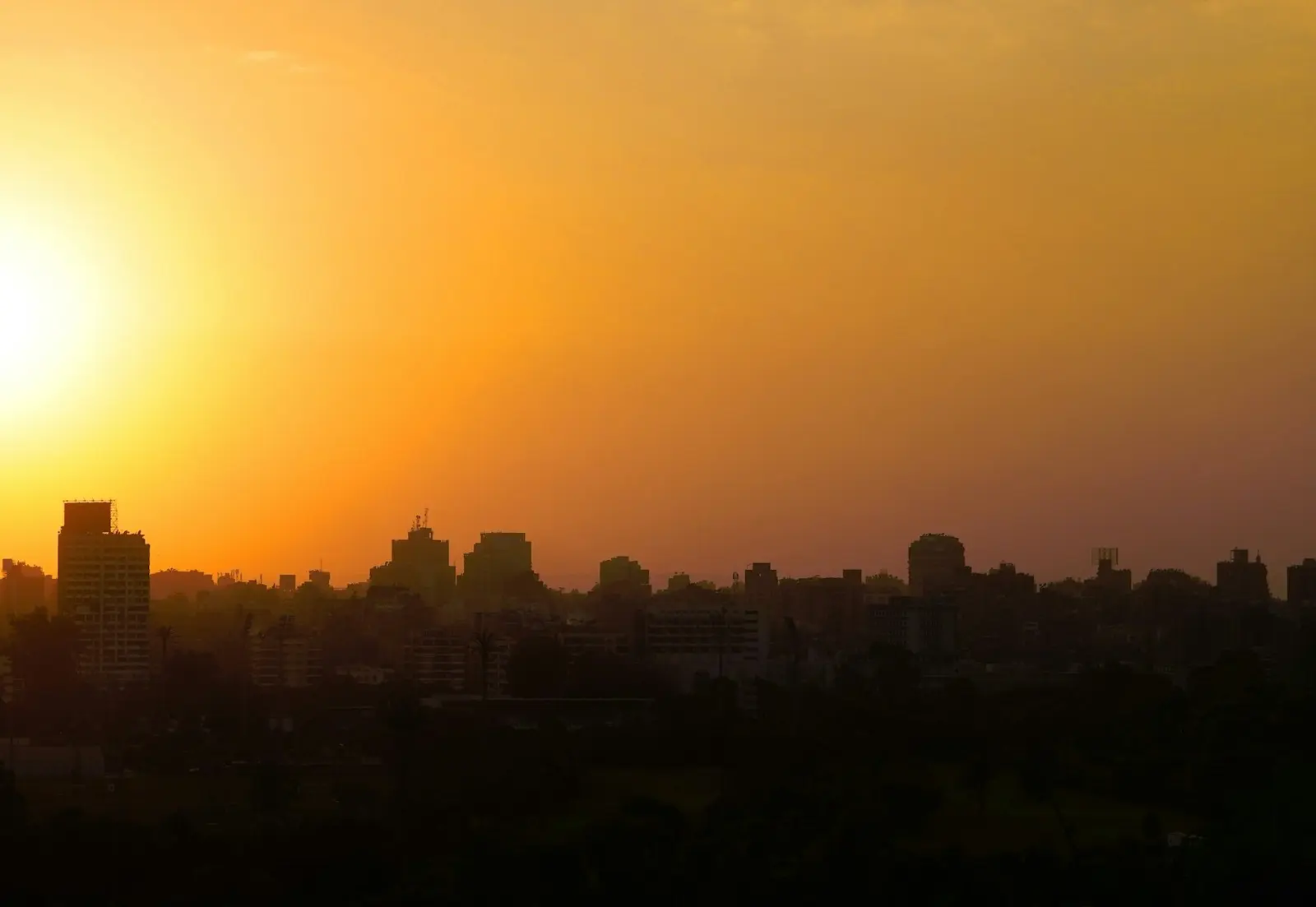 أفق القاهرة يرتسم ظلًّا داكنًا أمام سماء الغروب البرتقالية