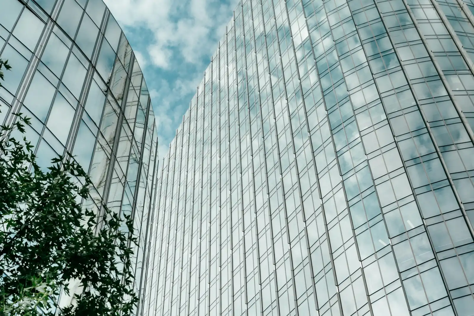 Curved glass office towers reflecting a blue sky with scattered clouds